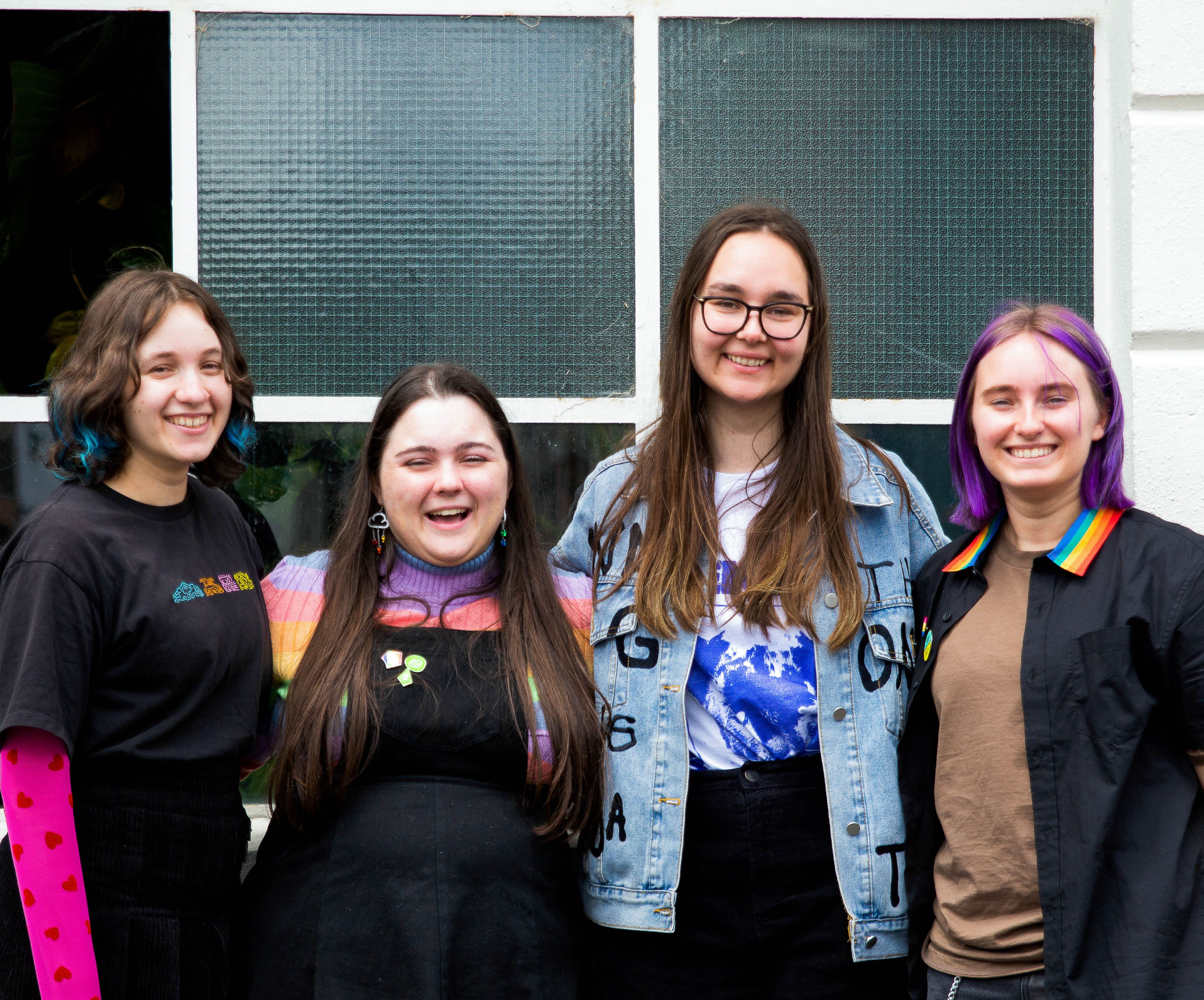 four teens smiling at camera in front of window