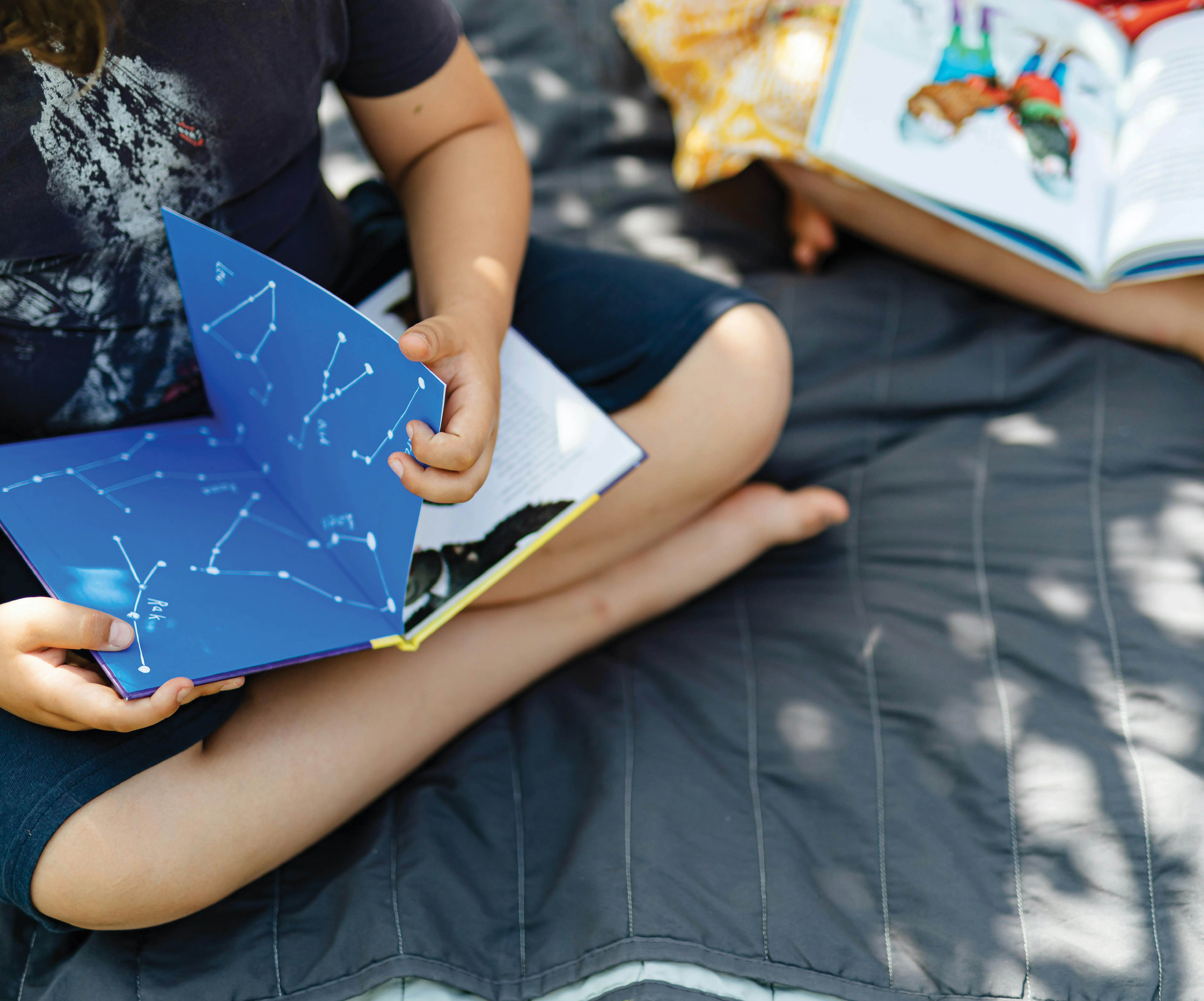 boy and girl reading on a blanket outdoors