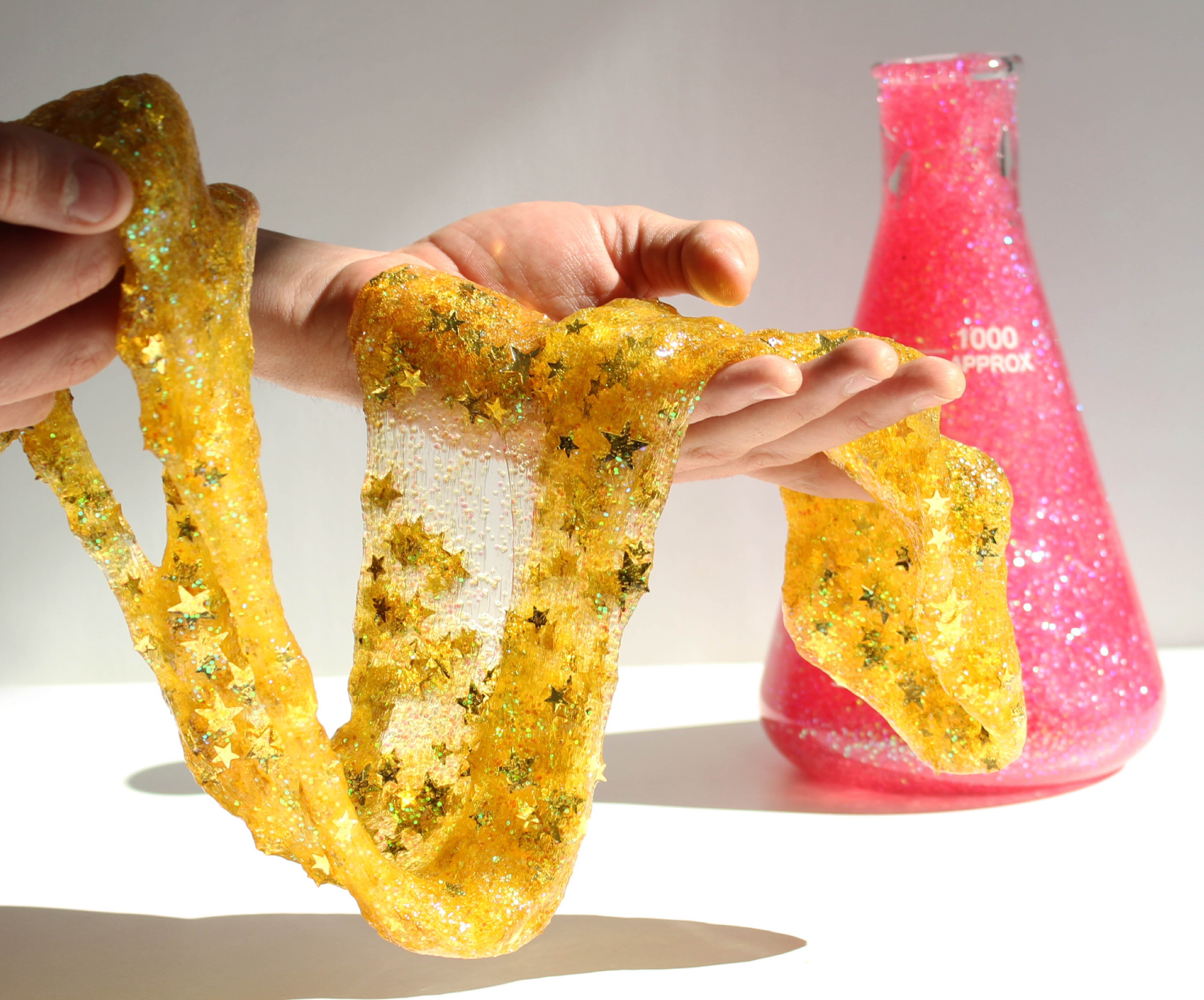 yellow sparkly slime and beaker filled with pink slime