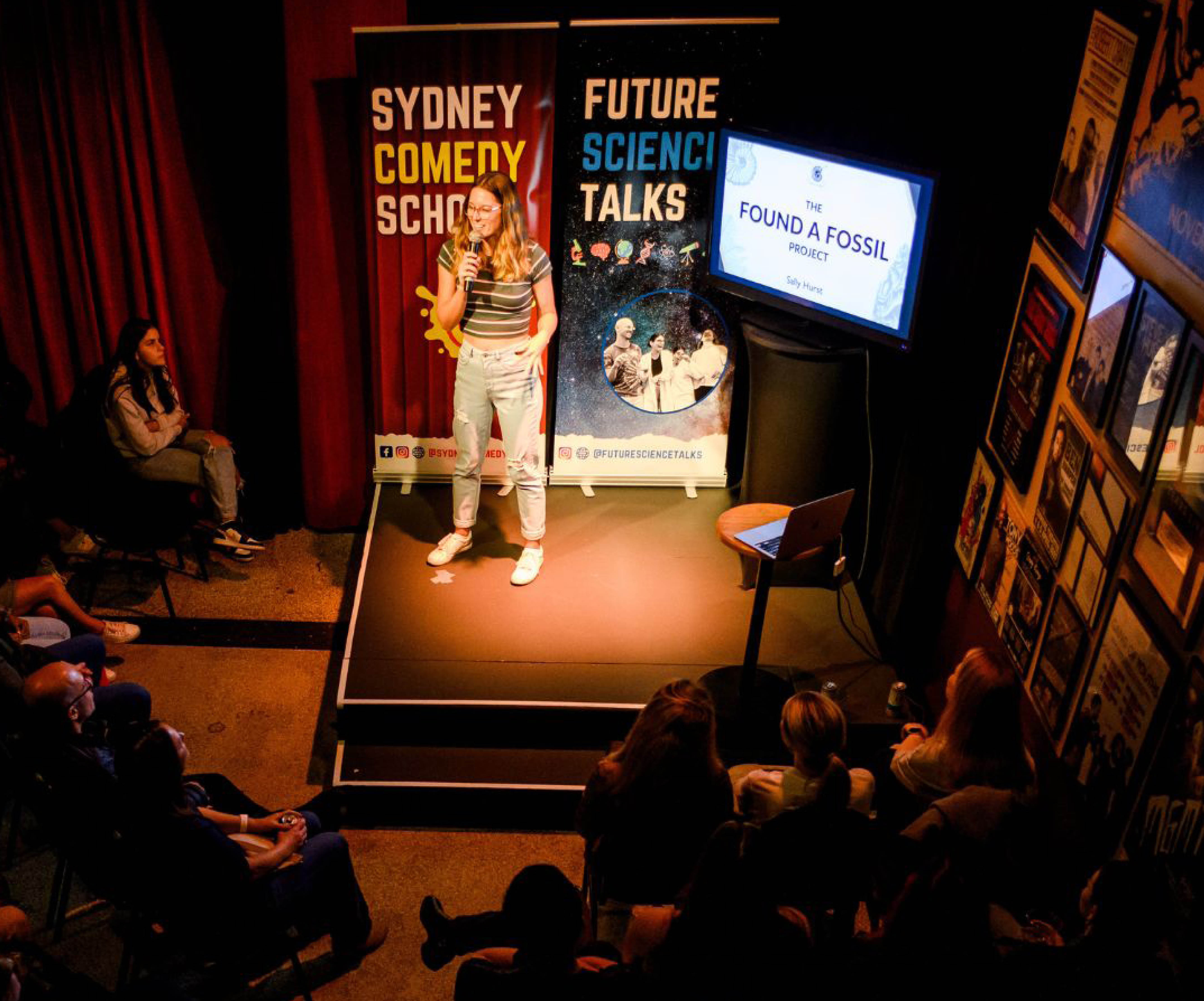 blonde girl on stage with screen and posters in background
