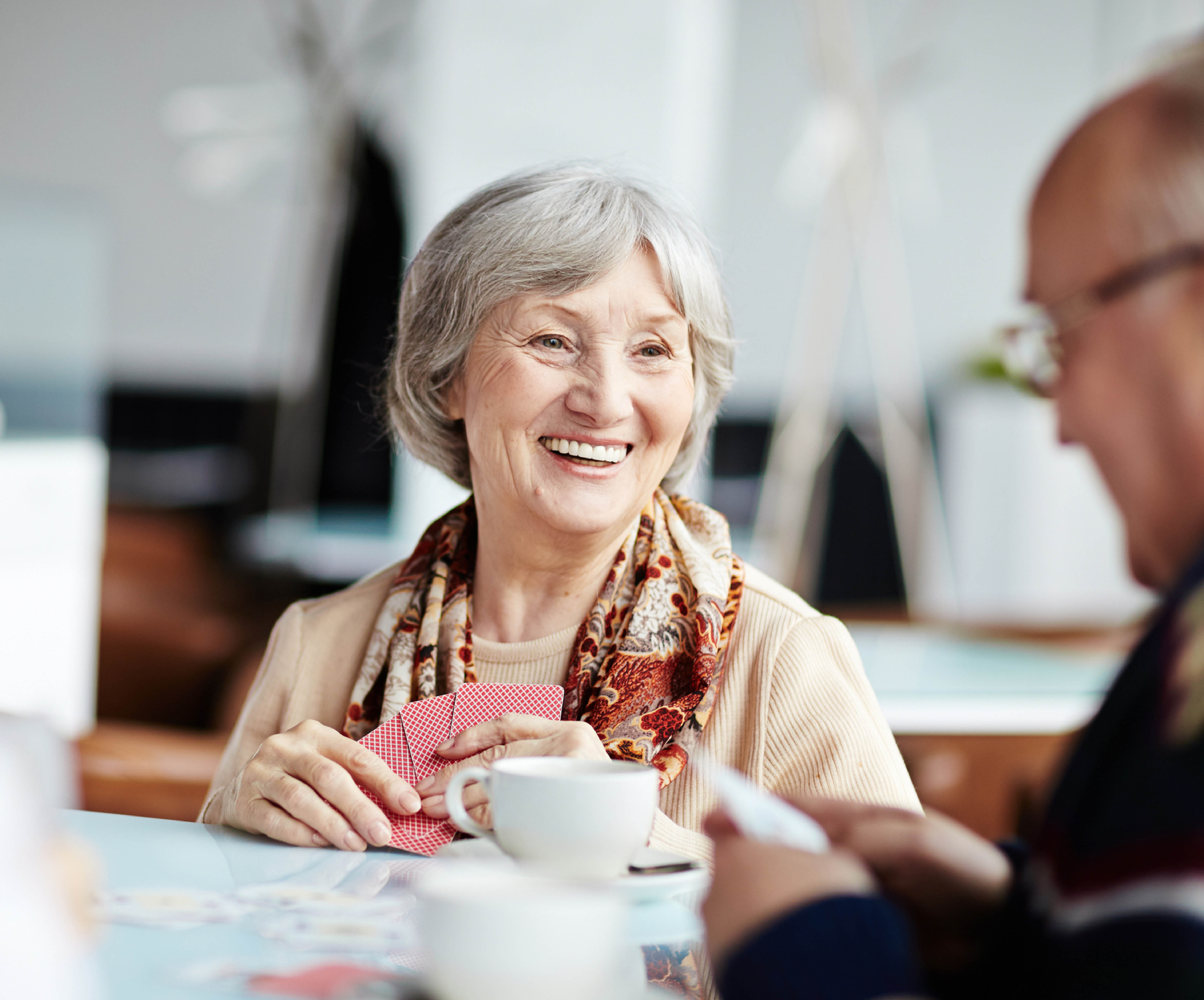 smiling lady wearing a scarf playing cards and drinking tea