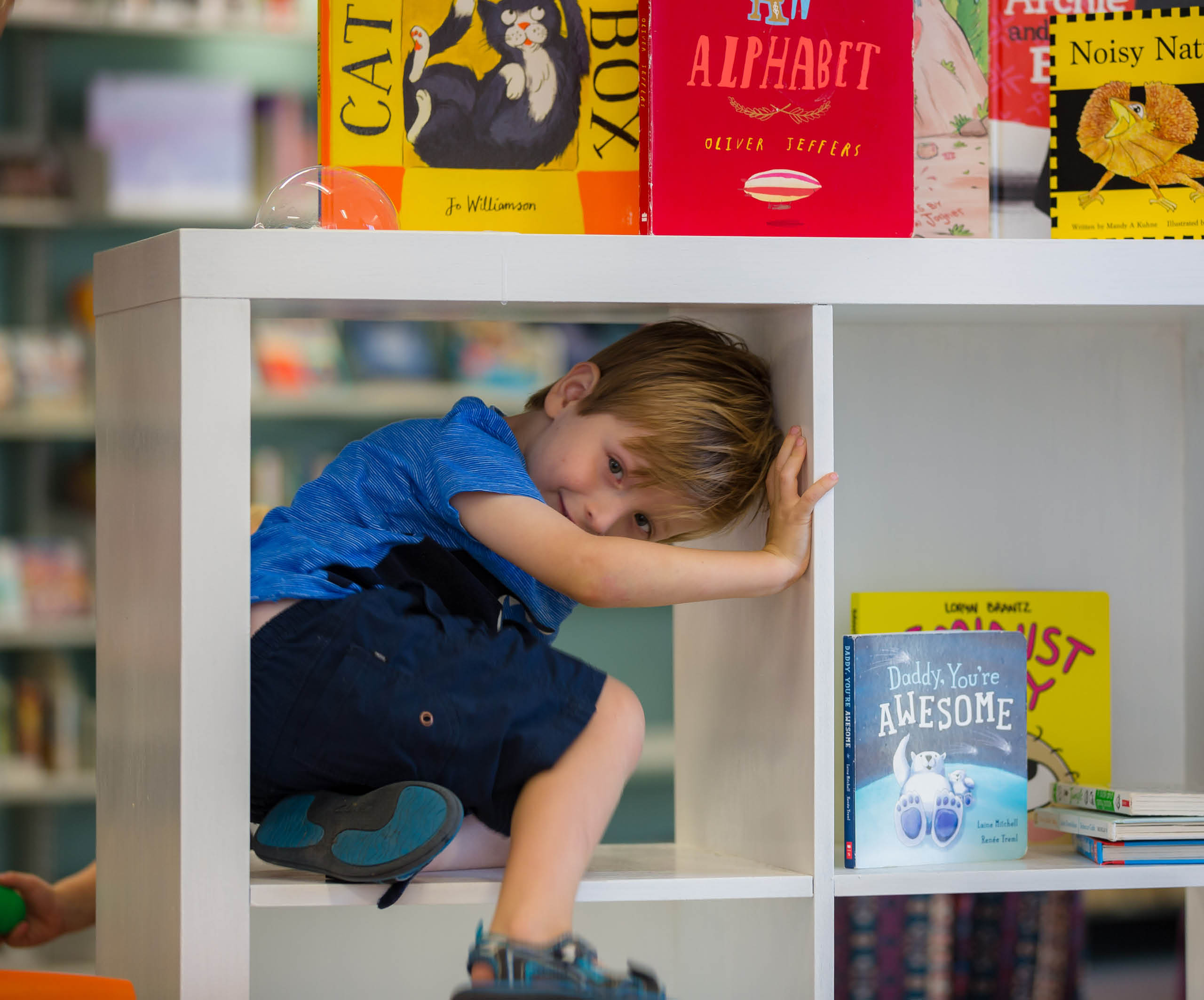 Blonde boy hiding in bookshelf sutherland library