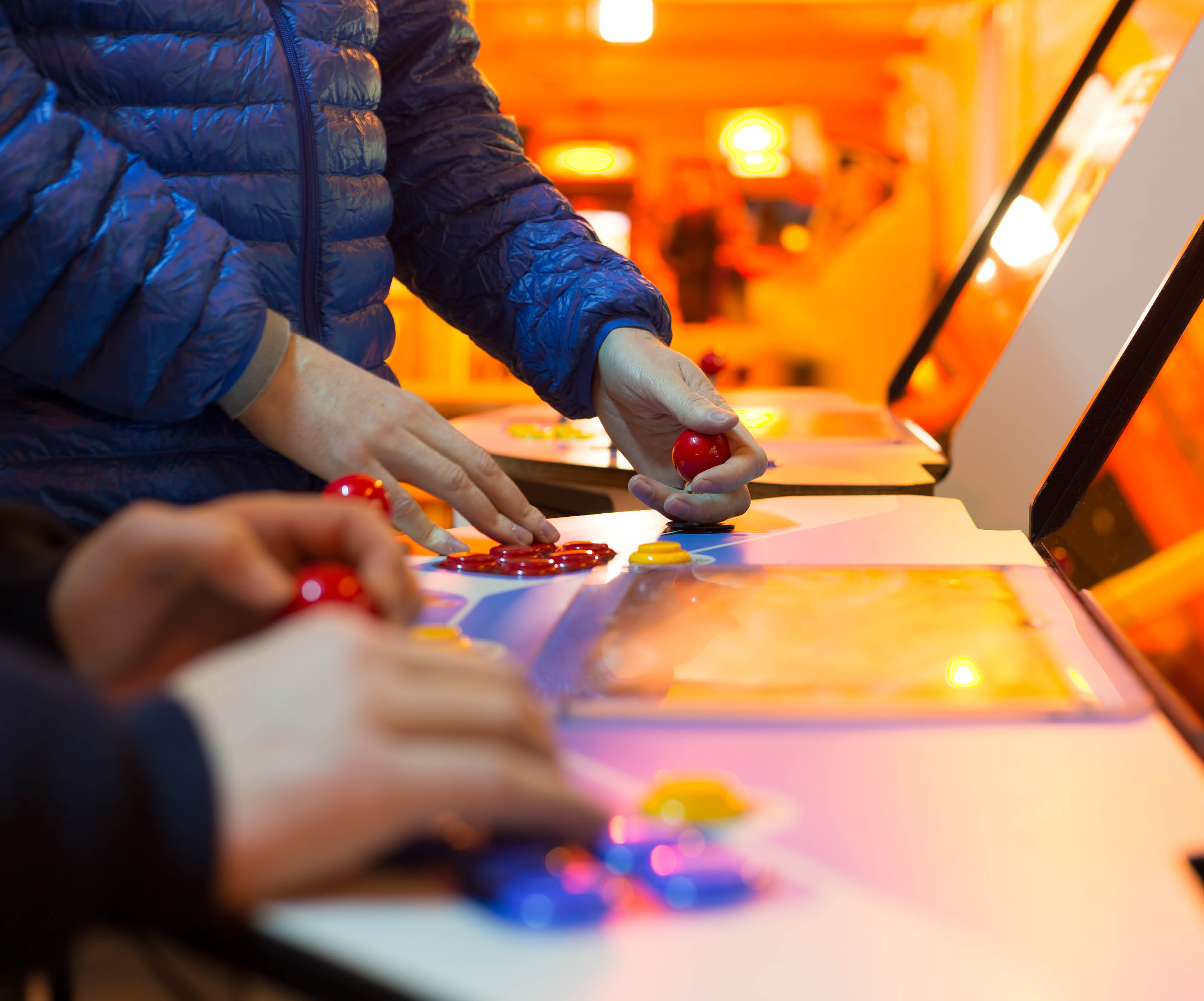two children's hands playing retro arcade machines